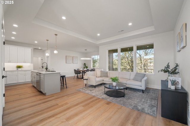 living room featuring sink, a tray ceiling, and light hardwood / wood-style flooring