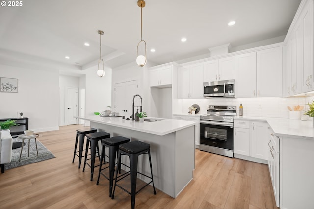 kitchen with appliances with stainless steel finishes, white cabinetry, an island with sink, sink, and hanging light fixtures