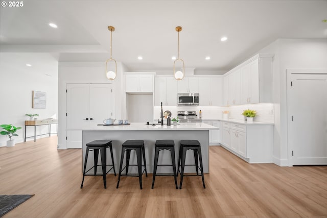 kitchen with appliances with stainless steel finishes, a kitchen island with sink, hanging light fixtures, backsplash, and white cabinets