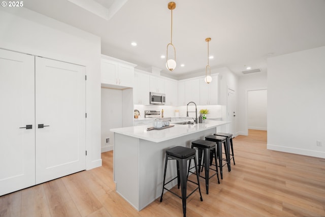 kitchen with white cabinetry, an island with sink, a kitchen breakfast bar, hanging light fixtures, and stainless steel appliances