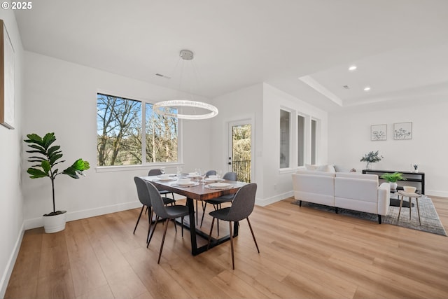 dining space with a notable chandelier, a tray ceiling, and light hardwood / wood-style flooring