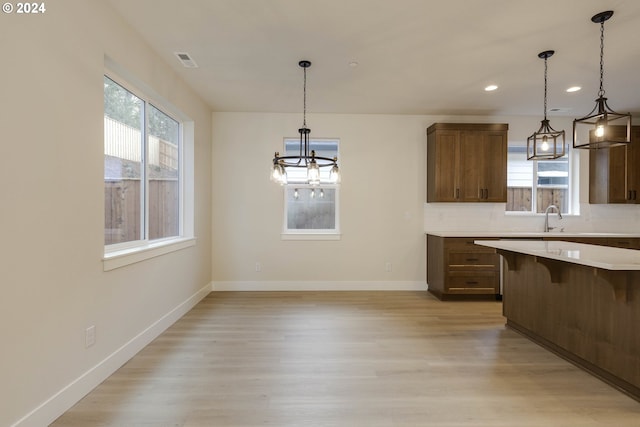 kitchen featuring light wood-type flooring, tasteful backsplash, decorative light fixtures, and a breakfast bar