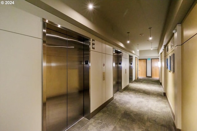 hallway featuring dark carpet, baseboards, and elevator