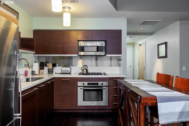 kitchen with appliances with stainless steel finishes, dark hardwood / wood-style floors, dark brown cabinetry, and sink