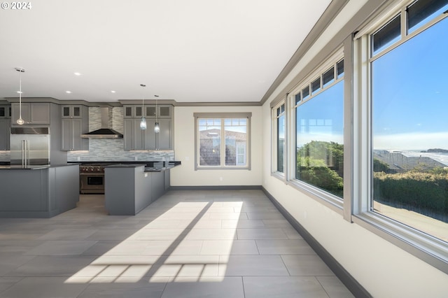 kitchen featuring wall chimney exhaust hood, gray cabinetry, ornamental molding, pendant lighting, and appliances with stainless steel finishes