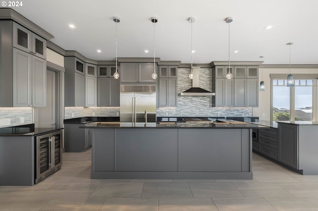 kitchen featuring tasteful backsplash, stainless steel built in fridge, wall chimney range hood, gray cabinets, and hanging light fixtures