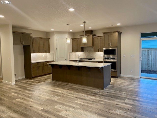 kitchen with pendant lighting, stainless steel appliances, light hardwood / wood-style floors, and a center island with sink