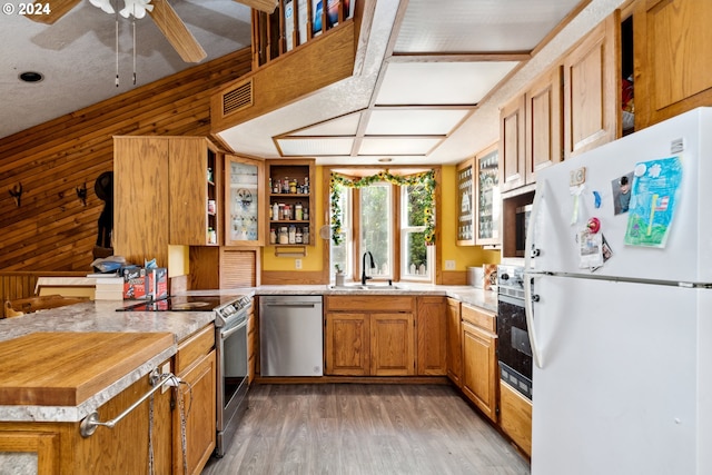 kitchen featuring stainless steel appliances, wood walls, sink, hardwood / wood-style floors, and kitchen peninsula