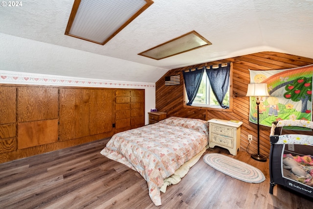 bedroom with dark wood-type flooring, wood walls, vaulted ceiling, and a textured ceiling