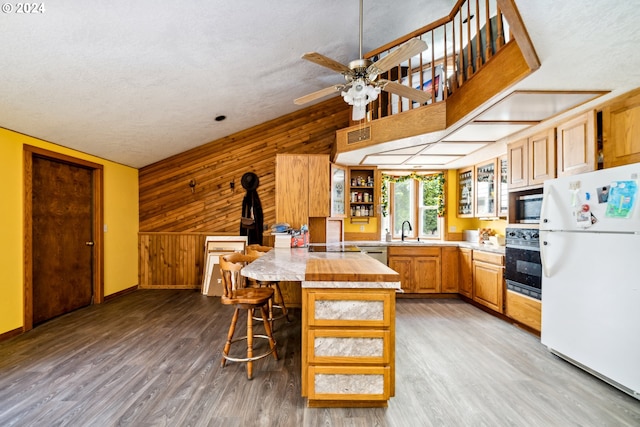 kitchen with stainless steel appliances, sink, light hardwood / wood-style flooring, a center island, and wooden walls