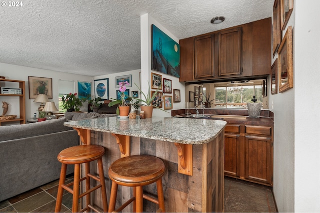 kitchen featuring dark tile floors, sink, a kitchen bar, light stone countertops, and a textured ceiling