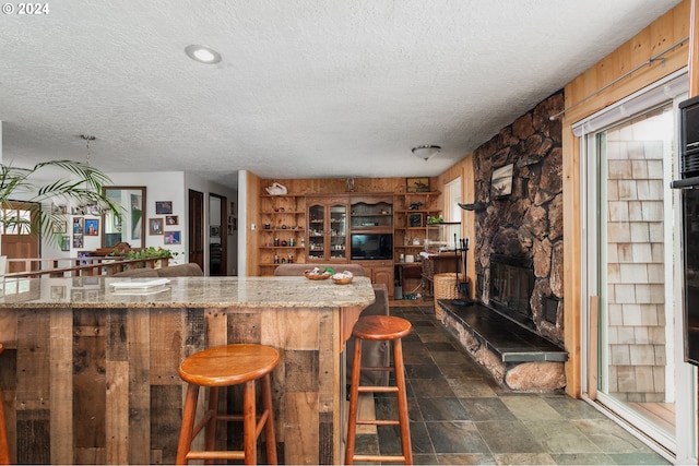 kitchen featuring a breakfast bar area, light stone countertops, a fireplace, and a textured ceiling