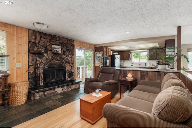 tiled living room with a fireplace, wood walls, a textured ceiling, and a healthy amount of sunlight