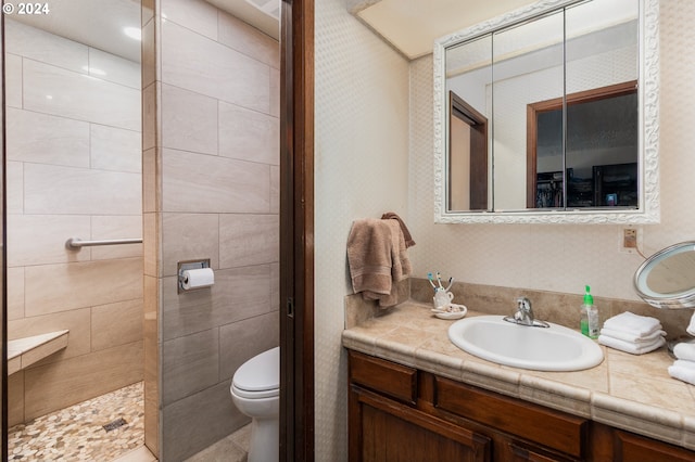 bathroom with toilet, a tile shower, and vanity