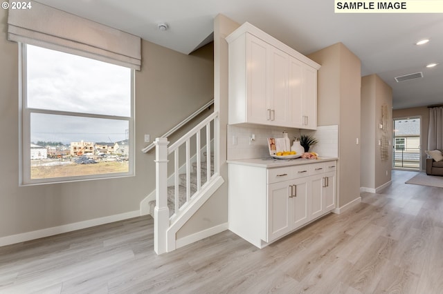 interior space with white cabinets, light wood-type flooring, and tasteful backsplash