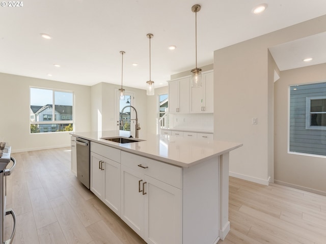 kitchen with appliances with stainless steel finishes, sink, a center island with sink, white cabinets, and hanging light fixtures