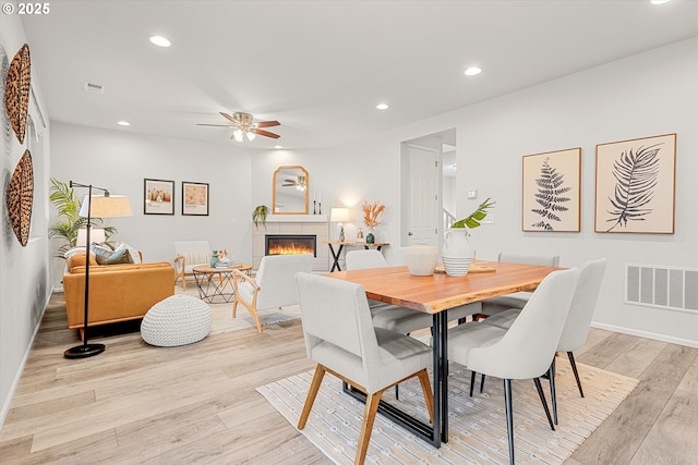 dining space featuring a tiled fireplace, ceiling fan, and light hardwood / wood-style flooring