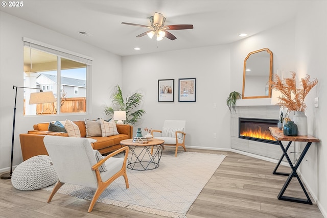 living room with light hardwood / wood-style floors, ceiling fan, and a tiled fireplace