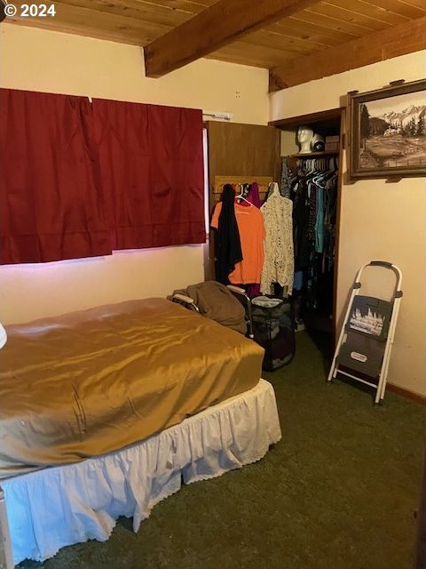 bedroom with a closet, beamed ceiling, wooden ceiling, and dark carpet