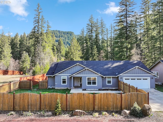 view of front of house featuring a shingled roof, an attached garage, board and batten siding, a fenced front yard, and driveway