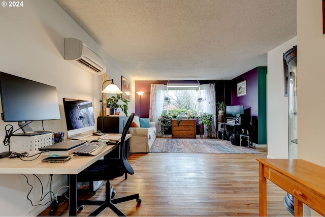 office with an AC wall unit, light hardwood / wood-style floors, and a textured ceiling