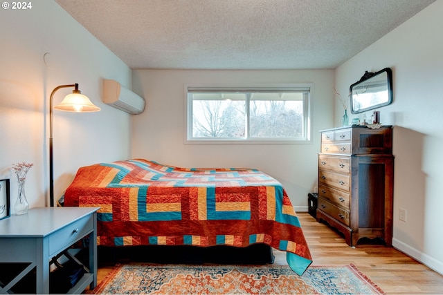 bedroom featuring a wall mounted air conditioner, a textured ceiling, and light wood-type flooring