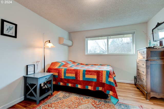 bedroom featuring a textured ceiling, light wood-type flooring, and a wall unit AC