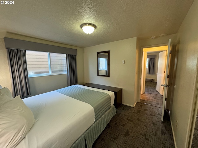 bedroom featuring a textured ceiling, a baseboard heating unit, and dark colored carpet