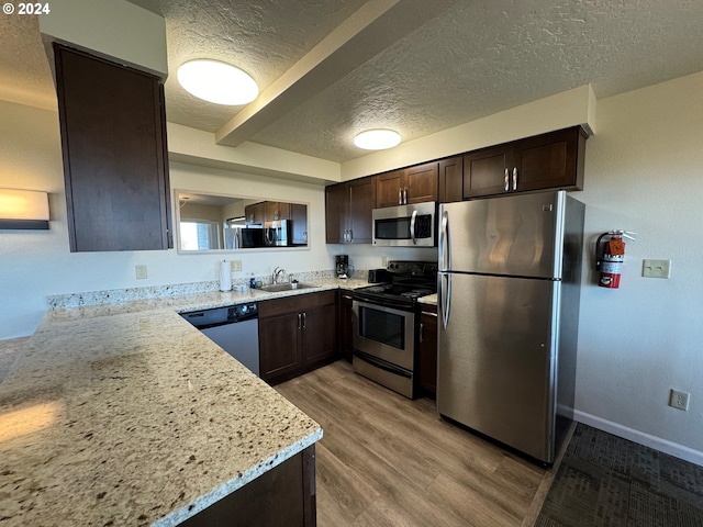 kitchen with a textured ceiling, stainless steel appliances, light hardwood / wood-style floors, sink, and light stone counters