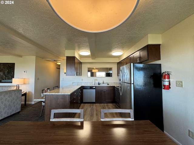 kitchen with light stone countertops, appliances with stainless steel finishes, sink, kitchen peninsula, and dark brown cabinets