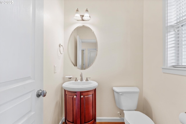 half bathroom featuring toilet, vanity, and baseboards