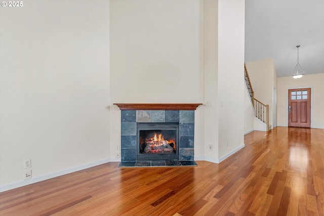 unfurnished living room with a tiled fireplace, stairway, a towering ceiling, and wood finished floors