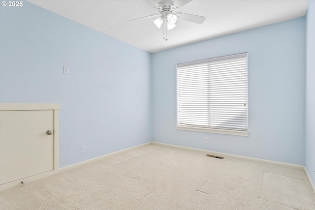 spare room with carpet flooring, a ceiling fan, visible vents, and baseboards