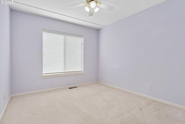 carpeted spare room with visible vents, baseboards, and ceiling fan