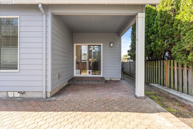 view of exterior entry with a patio area and fence