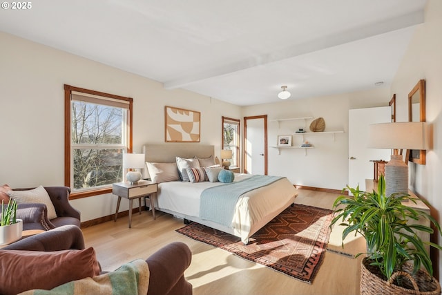 bedroom featuring light wood-type flooring, multiple windows, and beamed ceiling