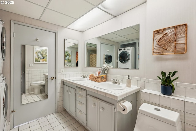 bathroom featuring stacked washer and clothes dryer, a paneled ceiling, tile patterned floors, and toilet