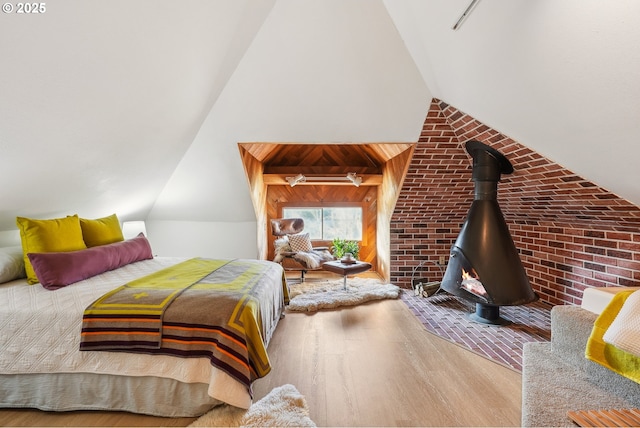 bedroom with brick wall, vaulted ceiling, a wood stove, and hardwood / wood-style flooring