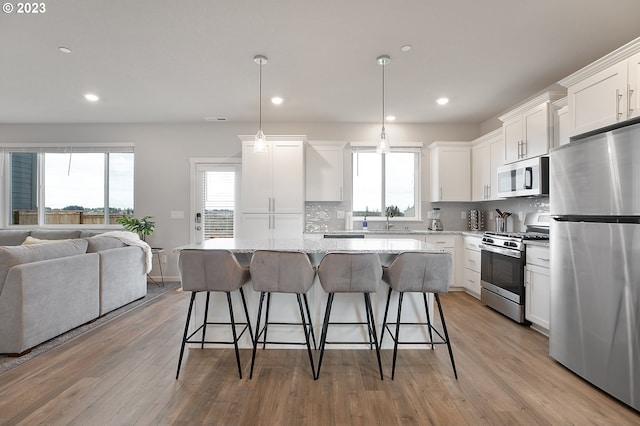 kitchen with light stone countertops, pendant lighting, white cabinets, appliances with stainless steel finishes, and a center island