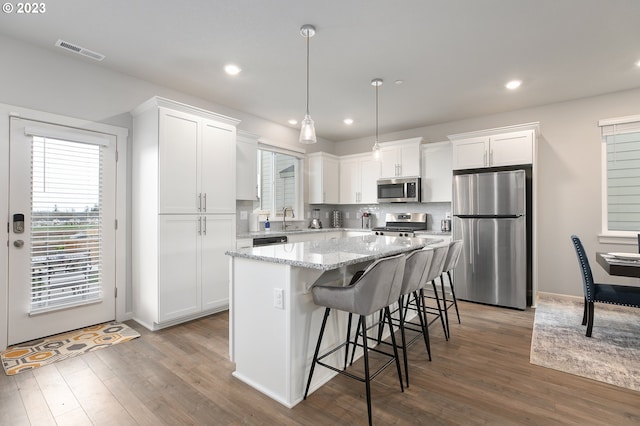 kitchen with pendant lighting, appliances with stainless steel finishes, a kitchen island, white cabinetry, and sink