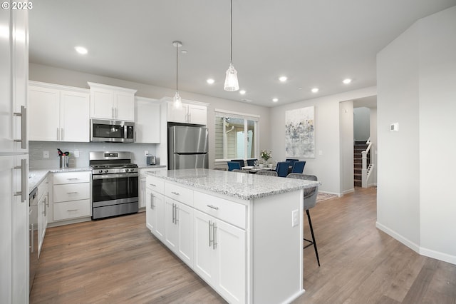 kitchen with a center island, appliances with stainless steel finishes, tasteful backsplash, white cabinetry, and pendant lighting