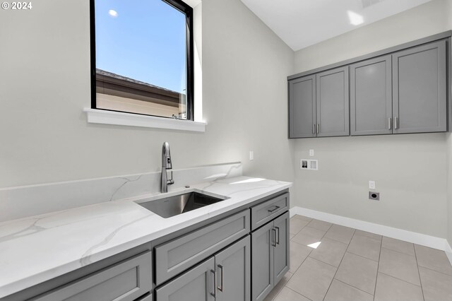 kitchen featuring gray cabinets, light stone counters, light tile patterned flooring, and sink