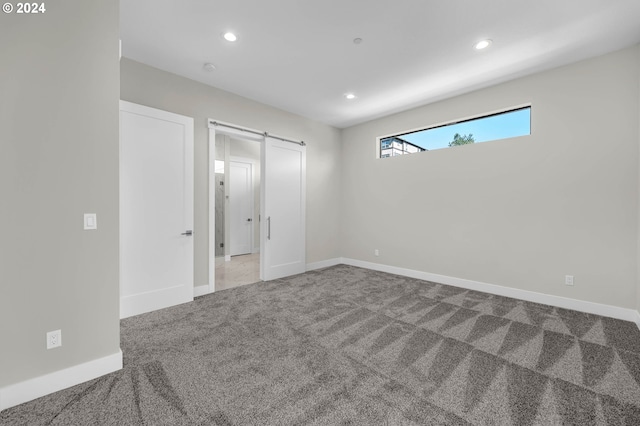 unfurnished bedroom featuring a barn door and light carpet