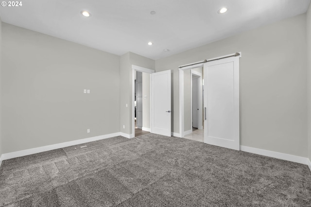 unfurnished bedroom with a barn door and light colored carpet