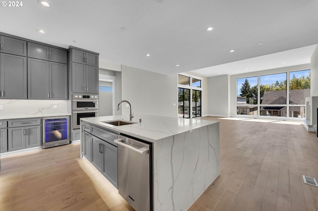 kitchen with an island with sink, light stone counters, wine cooler, and sink