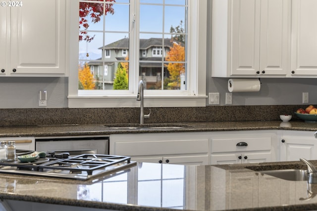 kitchen with stainless steel dishwasher, white cabinetry, dark stone counters, and sink