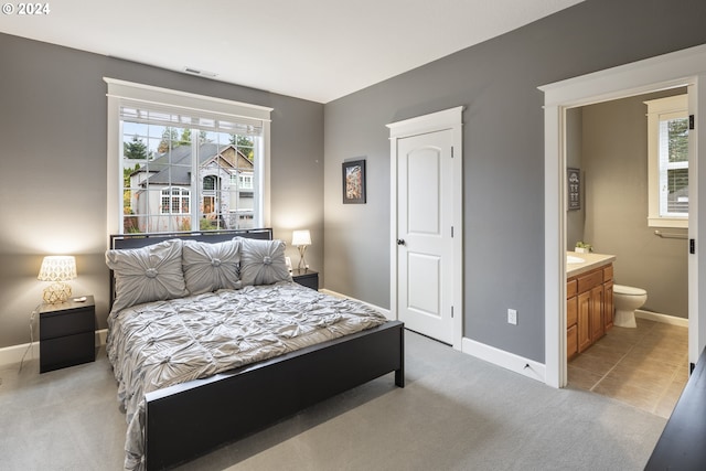 bedroom featuring ensuite bathroom, multiple windows, and light colored carpet