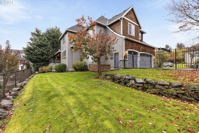 rear view of property featuring a garage, a yard, and a hot tub