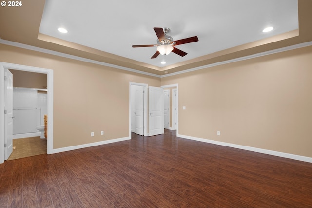 unfurnished bedroom featuring ensuite bath, dark wood-type flooring, ceiling fan, and a tray ceiling