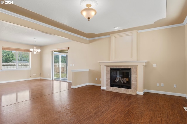 unfurnished living room featuring dark hardwood / wood-style flooring, a tiled fireplace, ornamental molding, and a notable chandelier